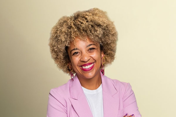 Alex West Steinman, a woman of color with a light brown afro and a pink blazer