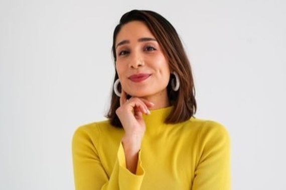 A professional photo of Arianna Genis, a Latina woman with shoulder length brown hair wearing a yellow shirt and hoop earrings. 