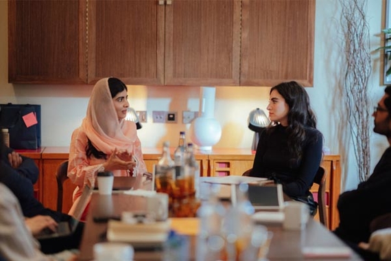 Malala Yousafzai, a young woman of color in a pink hijab sits with Arij Mikati, a woman of color in a black sweater