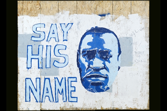 A portrail of George Floyd painted on plywood in tones of blue with the text "Say His Name" stacked along the left side of the portrait.