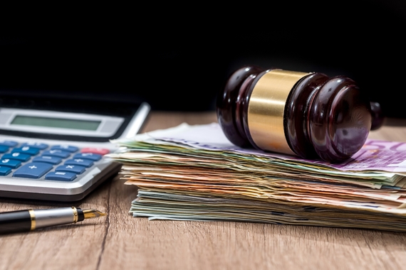 Gavel on top of pile of cash, next to a calculator and pen