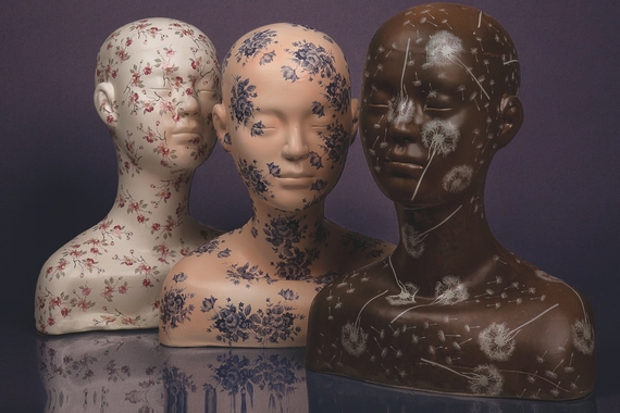 Three ceramic busts in white, cream, and brown skintones with floral decals all over their bald heads and shoulders