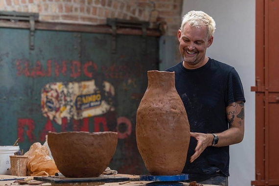 Smiling man stands next to large brown clay vases and bowls on a table