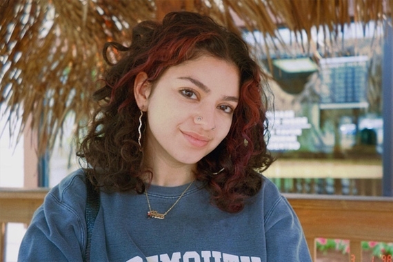 A young person with brown curly hair and red highlights smiles into the camera