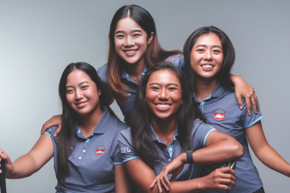 Four women in polos pose for a photo before a gray background