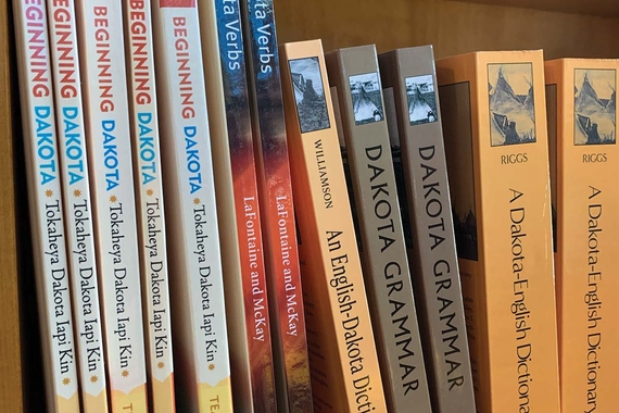 A close picture of a bookshelf holding several copies of books titled: "Beginning Dakota," "550 Dakota Verbs," "An English-Dakota Dictionary," and "Dakota Grammar" respectively.