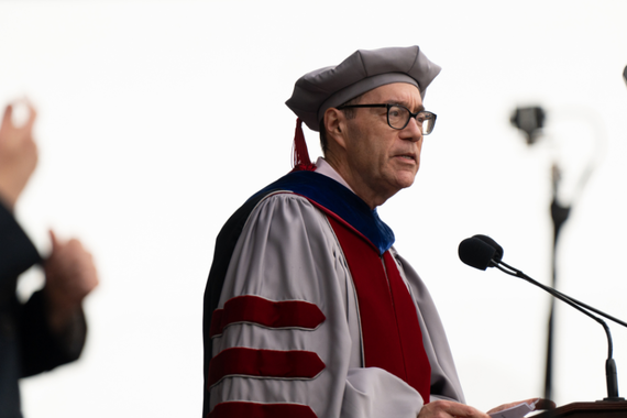 Dean Coleman wearing academic regalia addresses the crowd of students at commencement