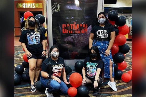 Four women wearing Robert Pattinson shirts and standing in front of The Batman movie poster at a movie theater
