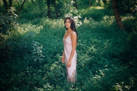 A woman in a pink satin dress stands in a lush green forest