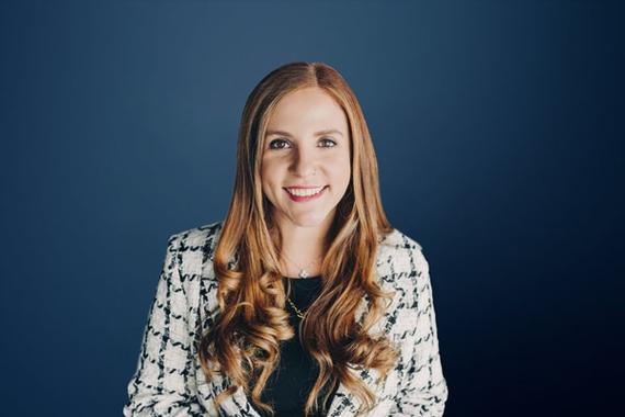 Erin Pash, a woman with long brown hair wearing a black-and-white patterned cardigan, in front of a navy blue background