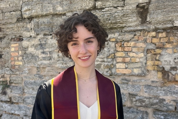 Photo of Fina Mooney in a graduation cap and gown in front of a brick wall.