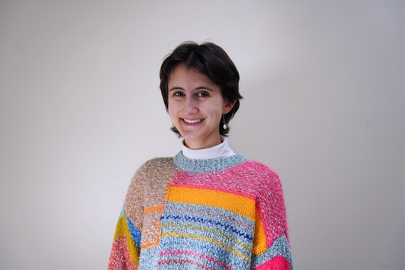 Madison Plemens-Schunk, wearing colorful sweater, stands in front of white background