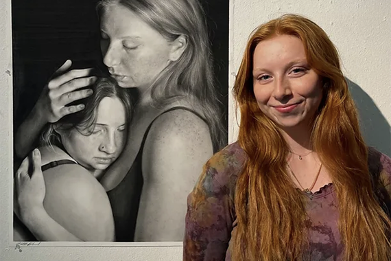 Smiling woman stands in front of realistic portrait of two women
