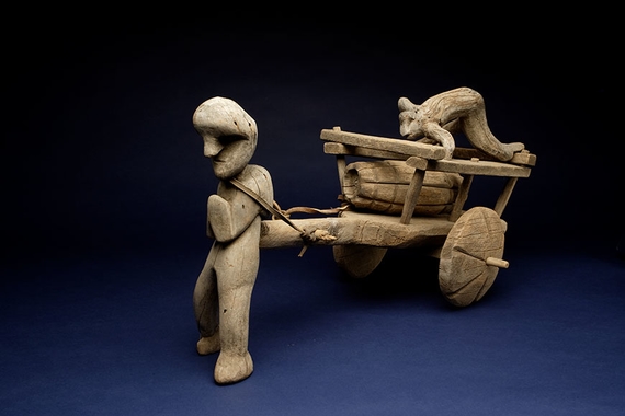 Carved wooden sculpture of a human figure pulling a cart