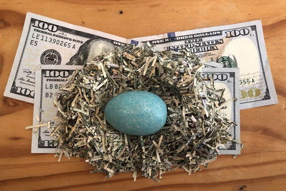 Blue egg nested in a bed of shredded paper, on top of a pile of $100 bills