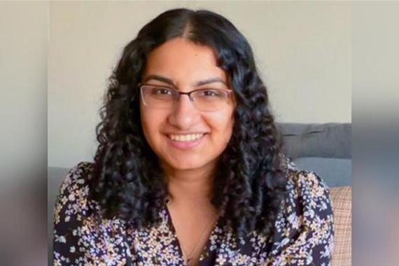 Nina Kaushikkar, a young woman of color with black hair wearing glasses and a floral shirt, smiles