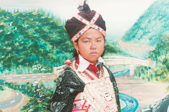 A Hmong woman in traditional garb in front of a landscape of rolling green hills