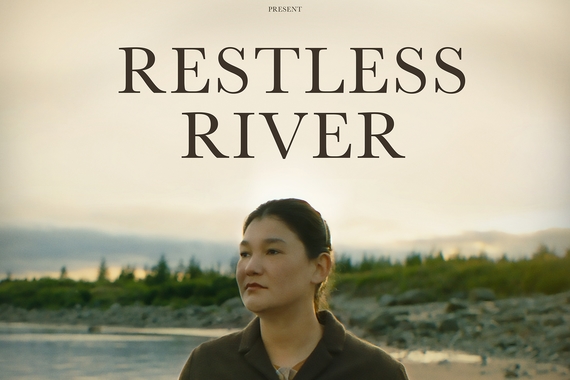 A photo of a woman standing on a beach with pine trees in the background. The words Restless River are displayed above her head