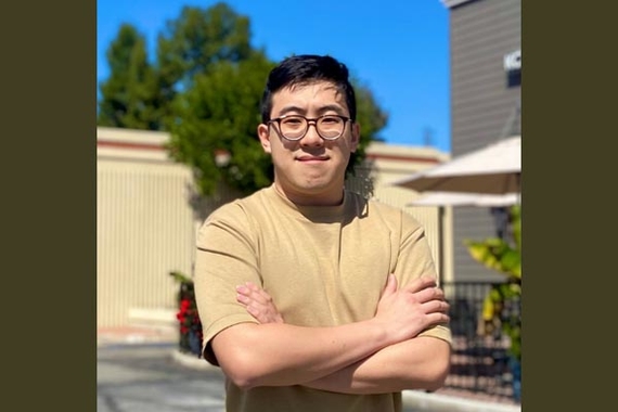 Richard Lim, a young man of color wearing glasses and a tan shirt, standing outdoors with his arms crossed