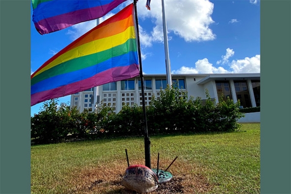 LGBTQ Pride flags and a rock with the words You Be You, in front of a Hagåtña, Guam government building