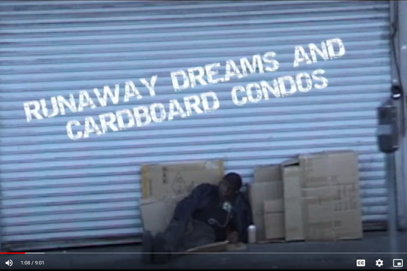 A man rests among a pile of cardboard boxes, a video screen grab from Runaway Dreams and Cardboard Condos
