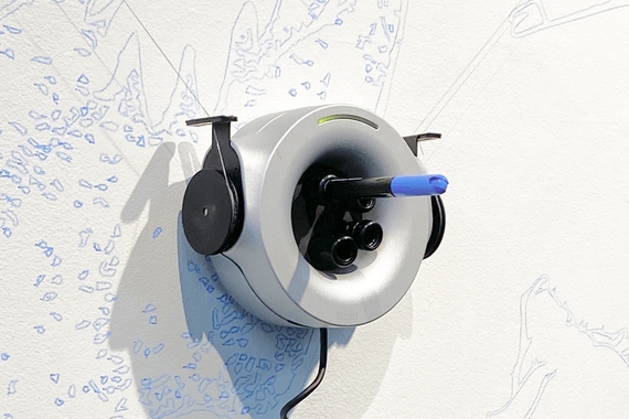 A suspended, circular machine uses a blue marker to draw on the wall