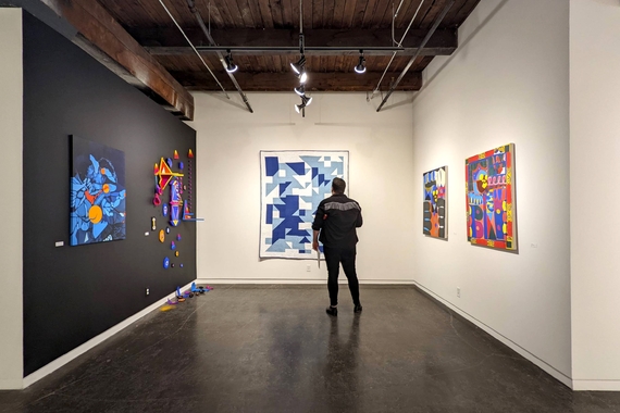 Installation view of artwork in Black Abstraction in the Midwest at SooVAC, with a person standing in front of a large blue and white quilt