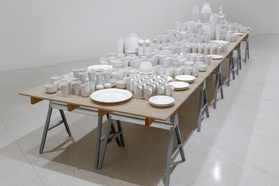 A table on sawhorses that is covered in white ceramic plates, bowls, cups, and vases