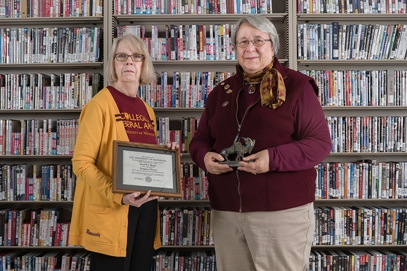 Two Alumnae stand in the East Asian library holding personal artifacts.