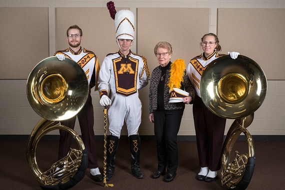Two tuba players, drum major and Jean Holten in a band practice room.