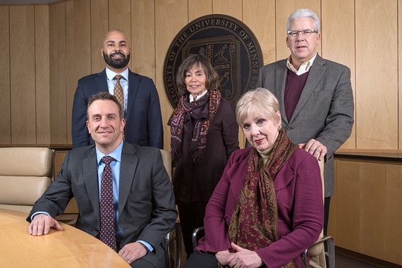The Provost and four of the Regents gather in the Regents board room in front of the University seal.