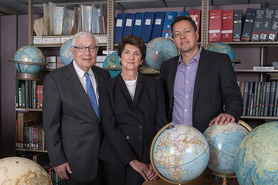 A couple stands with a faculty member in the basement of Wilson library surrounded by globes.