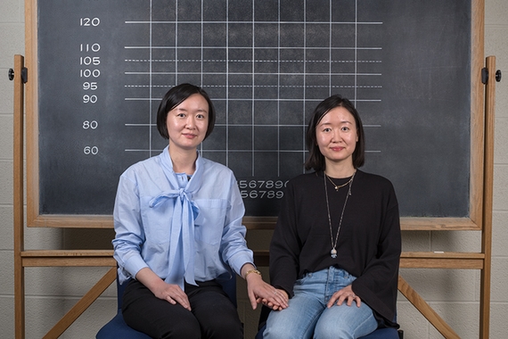 Li Wang and Chun Wang sitting in front of a blackboard, hand in hand
