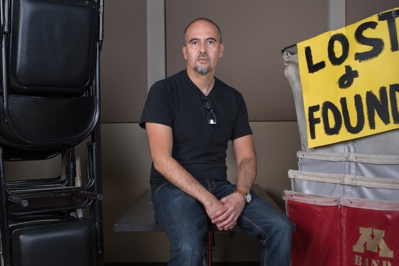 Photo of Xavier Tavera seated on a stool next to some rolling bins and a sign that says Lost and Found