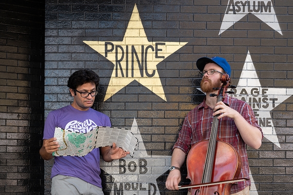 A man leans on First Avenue club wall near the prince star, while a student plays the cello.