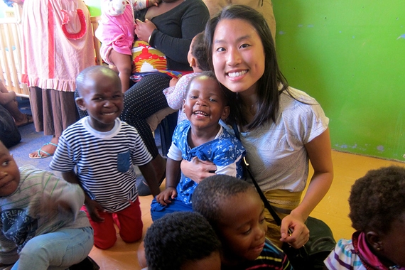 A student visiting a daycare in Khayelitsha Township, South Africa. She is seated with a small group of children. They are smiling.