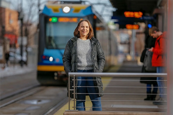 Photo of Alysha Alloway standing on a light rail train platform as a train approaches the station