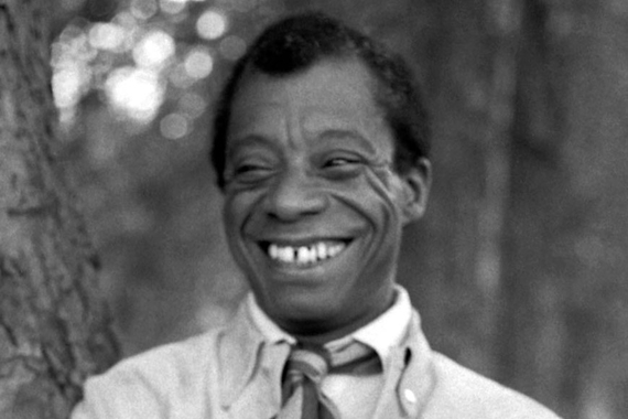 Black and white photo of American write and activist James Baldwin. He has a big smile in this photo.