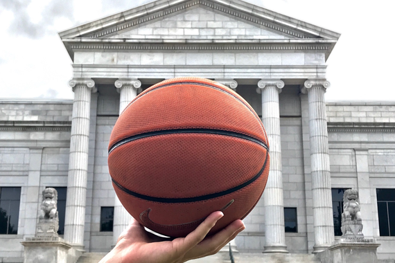 A basketball being held by a hand in front of the Minneapolis Institute of Art