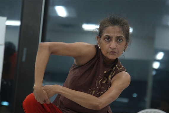 Photo of Ananya Chatterjea in a dance pose. She is crouching and her arms form a square shape.