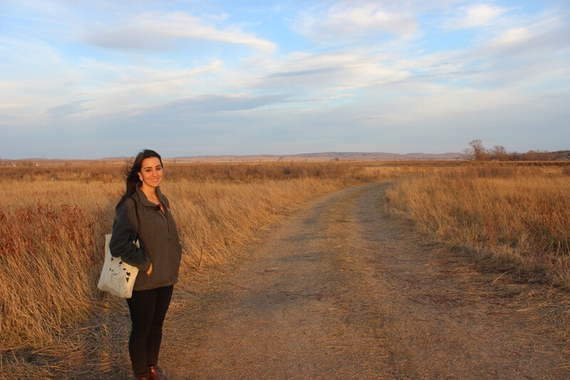 Caroline Doenmez, a young woman, standing on the side of a dirt road with dried grass on either side. The road is on the Standing Rock Indian Reservation. 