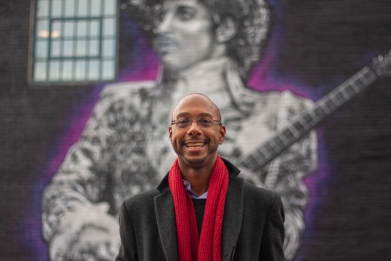 Elliot Powell stands in front of a mural of Prince. 