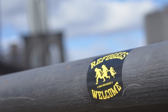 A sticker reading "refugees welcome" with outlines of a family running is placed on a bar in front of a fuzzy city background