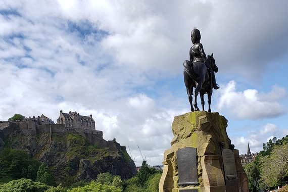 Photo of statue of man on hourse in foreground with castle on hill in back, surrounded by trees