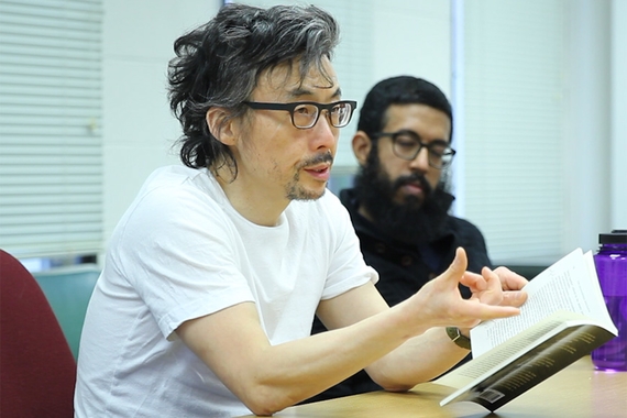 Professor Hoon Song speaking. A student in the background is listening.