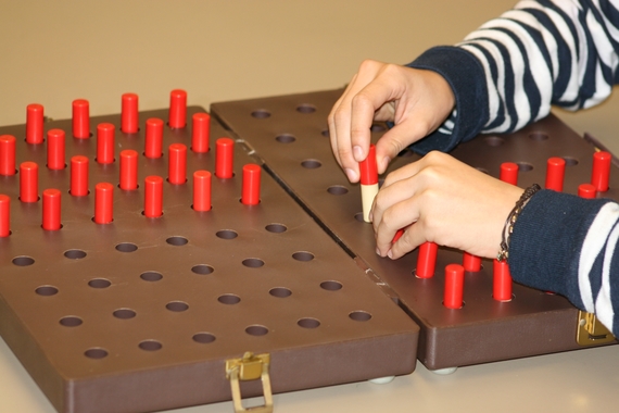 Hands moving pegs into holes on a board 