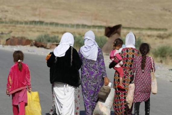 A group of 3 Iraqi women and 3 girls carrying bags and walking on a road away from the camera