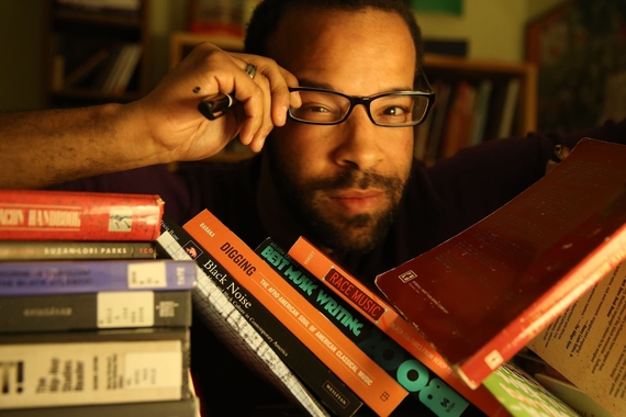Doug Kearney peering through a shelf of books, grabbing at his glasses and squinting
