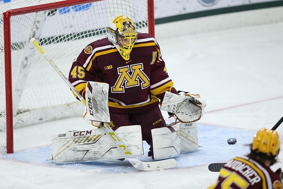 Photo of Gopher hockey goalie Jack LaFontaine in goalie pads in front of goal with hand out as black puck flies in from bottom right