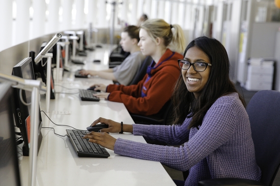 A student smiling at the camera while working at a computer.